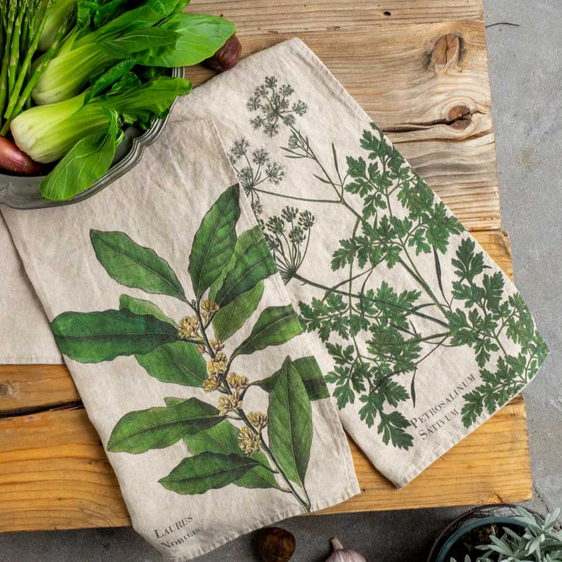 Two botanical-themed towels on a wooden cutting board with fresh vegetables.