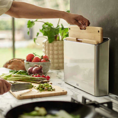 Person preparing vegetables on a cutting board with a knife block in the background